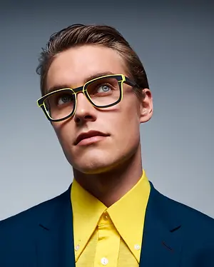 A man with brown hair wearing yellow glasses and a yellow shirt and blue blazer