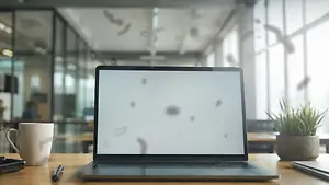 An open laptop is placed on a wooden table, which is in an office space. There is a potted plant, a cup, and a pen on the table. The laptop screen is blurry, and the glass wall of the office space has some designs on it. There is a person standing behind the glass wall. There are other people in the office space, and the ceiling has lights.