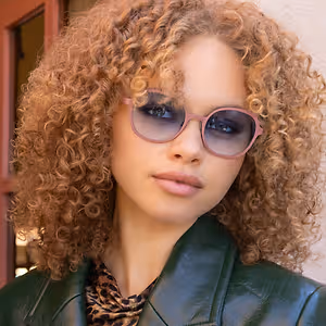 Woman with curly hair wearing pink sunglasses and a green jacket
