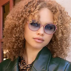 Woman with curly hair wearing pink sunglasses and a green jacket