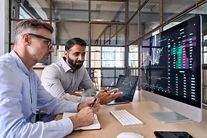 Two men sitting in an office and analyzing charts on a computer screen