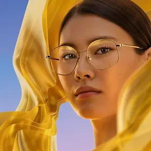 A woman wearing glasses and a yellow dress with her head slightly tilted and her eyes closed