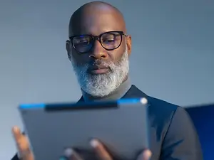 A bald man with a white beard is looking at a tablet device