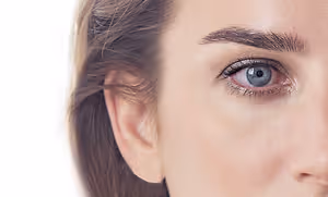 Close up of a woman with light brown hair, blue eyes, and black eyeliner on a white background