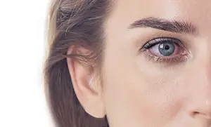 Close up of a woman with light brown hair, blue eyes, and black eyeliner on a white background