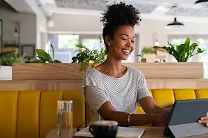A woman sitting at a table in a restaurant booth, smiling while using a tablet.