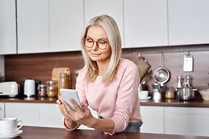 Woman wearing eyeglasses and holding a tablet while smiling in a kitchen