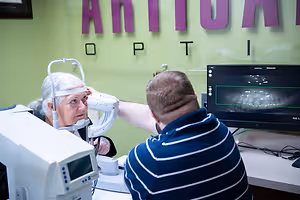 Optometrist examining a patient's eye with diagnostic equipment while an eye scan displays on a monitor