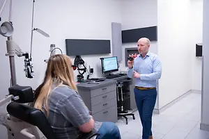 Optometrist demonstrating an eye examination device to a seated patient in an exam room