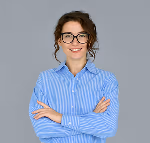 A woman in a blue striped shirt and glasses with her arms folded and smiling