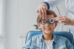 A young boy in a denim shirt getting his eyes examined by a doctor.