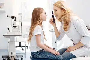 A young girl is having her eyes examined by a female doctor in a white lab coat in a medical clinic.