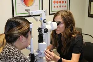 A woman is using an ophthalmoscope to check the eyes of another woman.