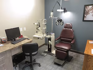 An optometrist's office with an eye examination machine and a desk with a computer monitor and keyboard.