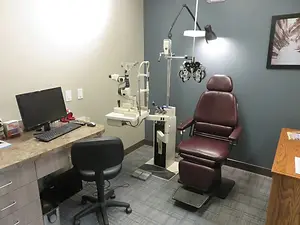 An optometrist's office with an eye examination machine and a desk with a computer monitor and keyboard.