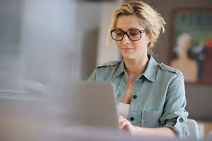 Blonde woman with glasses working on a laptop
