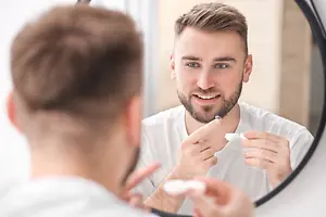 A man brushing his teeth while looking at his reflection in a mirror