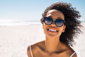 African American woman on the beach smiling with sunglasses on