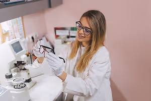 woman wearing a lab coat and glasses inspecting a pair of glasses