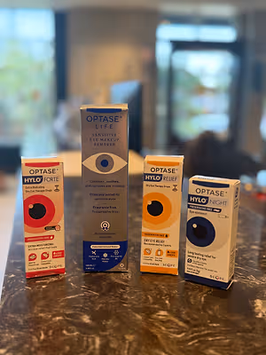 Four boxes of eye drops are on a marble surface, including the Optase Life, Optase Hylo Forte, Optase Hylo Relief, and Optase Hylo Night.