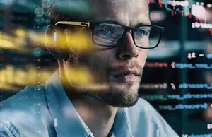 Man with glasses and headphones looking at a computer screen