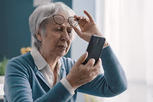 An older woman wearing glasses is holding a smartphone and adjusting her glasses.