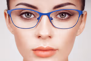 Close-up of a woman's face with blue glasses, her eyes slightly closed, and a slight smile