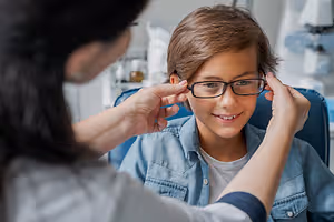 A young boy is getting his glasses adjusted by an optometrist in an office.