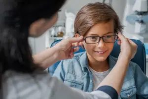 A young boy is getting his glasses adjusted by an optometrist in an office.