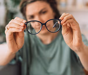 Woman holding glasses with a thoughtful expression