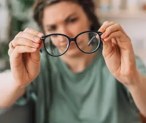 Woman holding glasses with a thoughtful expression