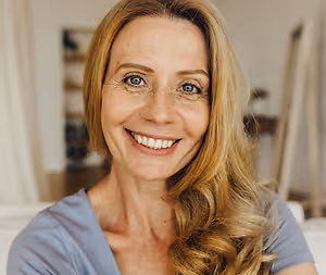 A woman with blonde hair and a blue shirt smiling at the camera in a room