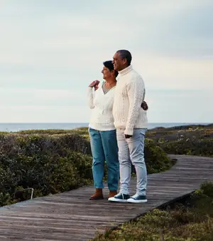 A couple stands on a wooden pathway in a scenic outdoor area near a body of water