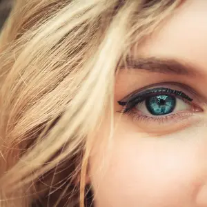 Close-up of a woman with blonde hair and blue eyes wearing makeup and smiling