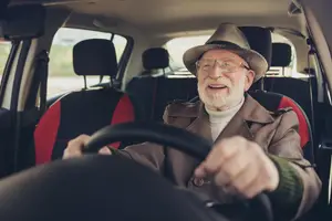 Senior man smiling and driving a car while looking at the side mirror