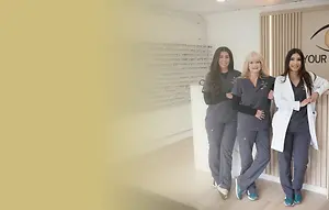 Three women wearing grey uniforms and lab coats are standing next to each other in a room