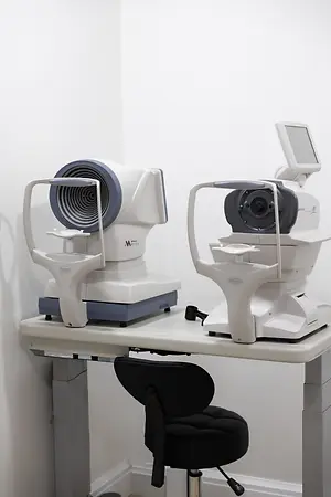 Two automated eye examination machines on an optometry table with a black patient stool