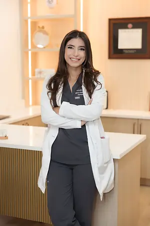 Smiling female optometrist in a white coat standing with folded arms in a clinic