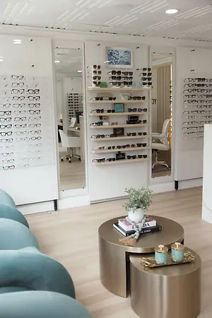 Bright optometry eyewear showroom with glasses displays, mirrors, seating, and a coffee table