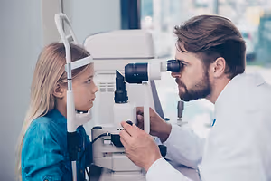 A doctor examining a young girl's eyes with a microscope in an eye clinic.