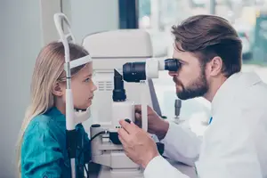 A doctor examining a young girl's eyes with a microscope in an eye clinic.