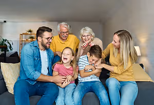 A family of five is sitting on a couch, smiling and laughing