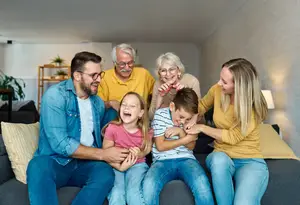 A family of five is sitting on a couch, smiling and laughing