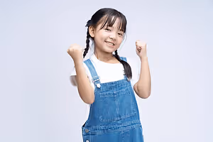 Happy young girl wearing blue overalls with her fists up