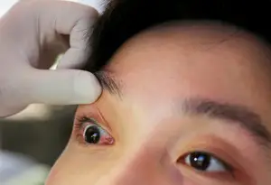 A doctor is adjusting the eyebrow of a person in an indoor area.