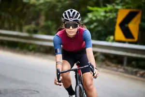A woman wearing a helmet and sunglasses rides a bicycle on a road with a yellow sign