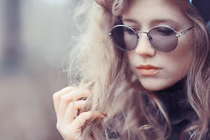 A young woman with long blonde hair wearing sunglasses and a black turtleneck poses for a photo