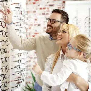 A family of three standing in front of a display of glasses and smiling at the camera