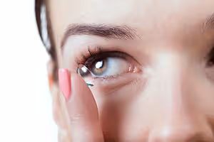 Close up of a woman with pink nails putting in a contact lens.