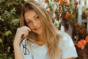 A woman is wearing a white shirt and holding glasses in her right hand and posing for a photo.